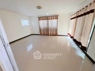 Spacious empty living room with large windows and tiled flooring.