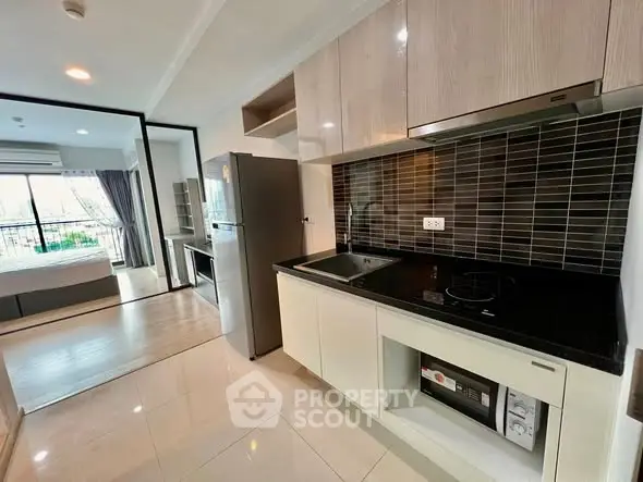 Modern kitchen with sleek appliances and open layout leading to a bright bedroom with balcony view.
