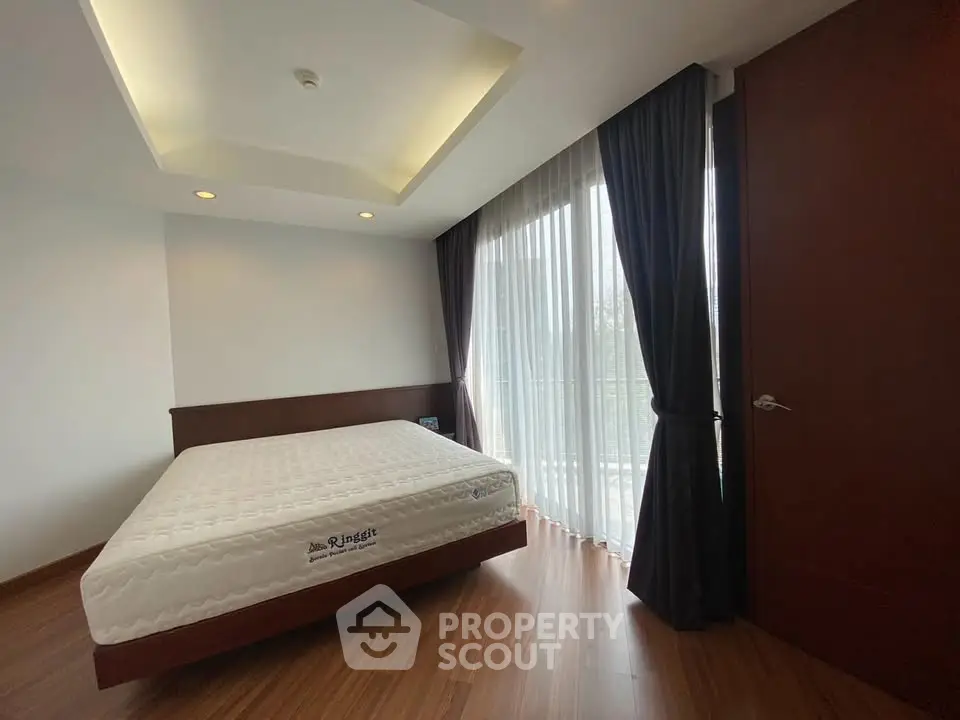 Spacious bedroom with large windows and elegant curtains in modern apartment.