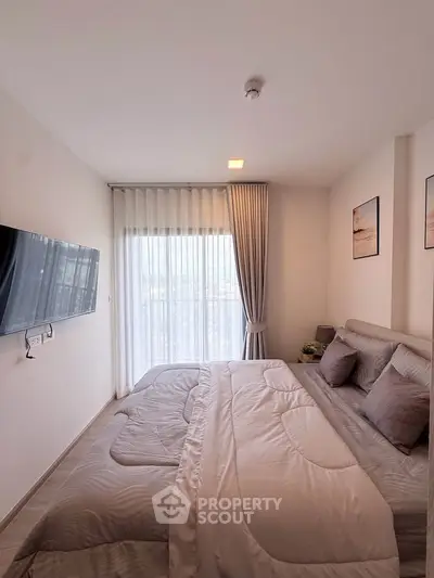Cozy modern bedroom with large window and wall-mounted TV, perfect for relaxation.