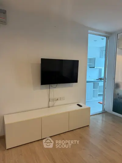 Modern living room with wall-mounted TV and sleek cabinet, leading to a bright kitchen area.