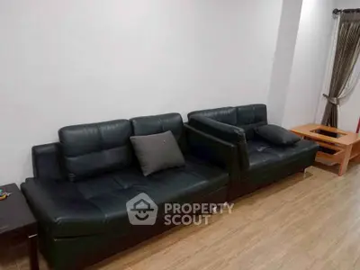 Spacious living room with black leather sofas and wooden flooring