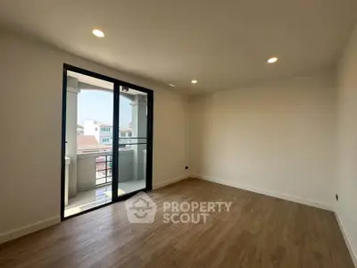 Spacious empty room with wooden flooring and large window leading to a balcony, perfect for customization.