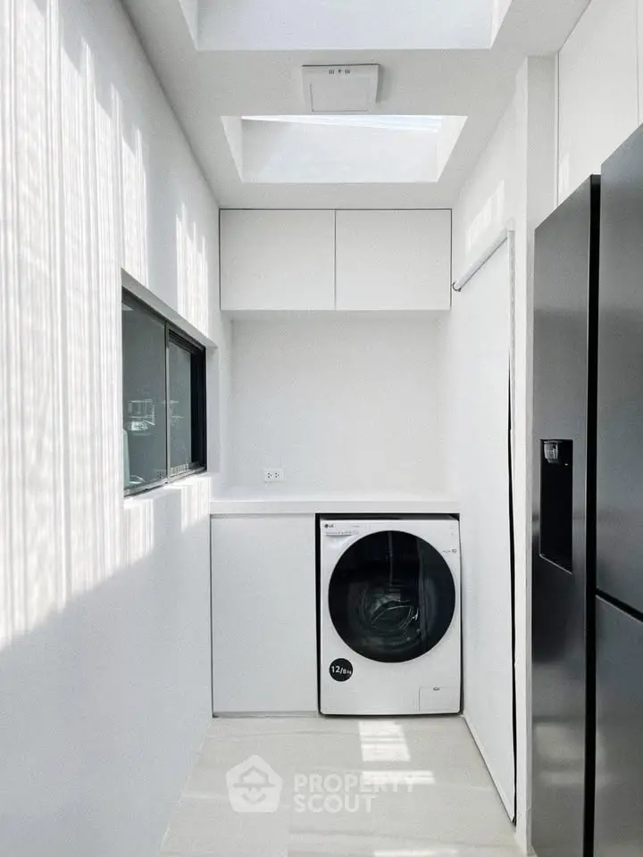 Modern laundry room with skylight, featuring a sleek washing machine and ample storage cabinets.