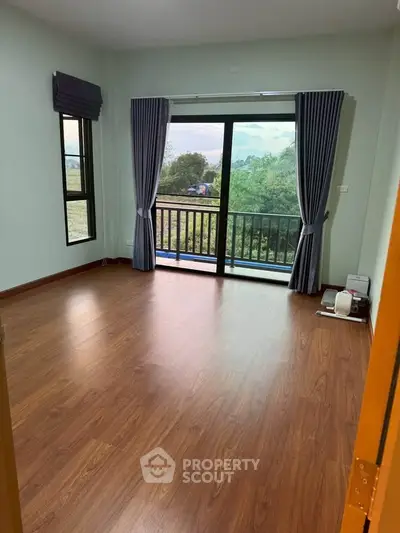 Spacious room with wooden flooring and large window offering scenic views, perfect for a cozy living space.