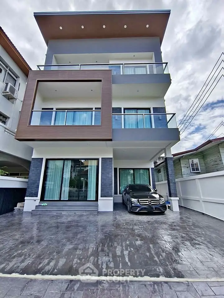Modern three-story house with spacious driveway and luxury car parked in front, showcasing contemporary architecture.