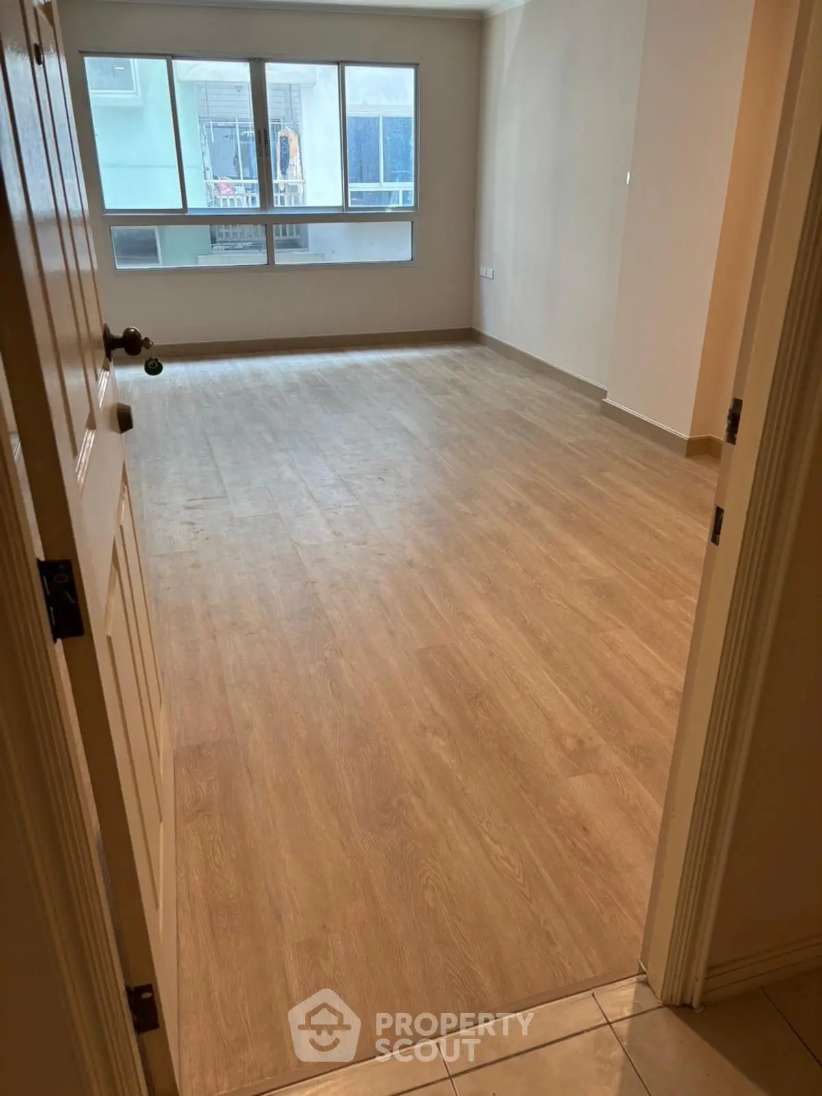 Spacious empty room with wooden flooring and large window, ideal for customization.