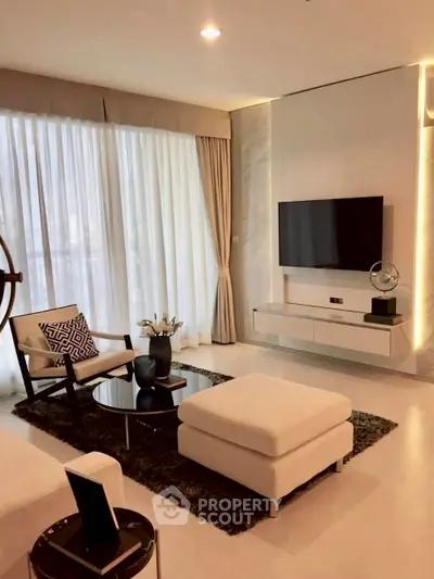 Modern living room with elegant decor, featuring a wall-mounted TV and large windows with sheer curtains.