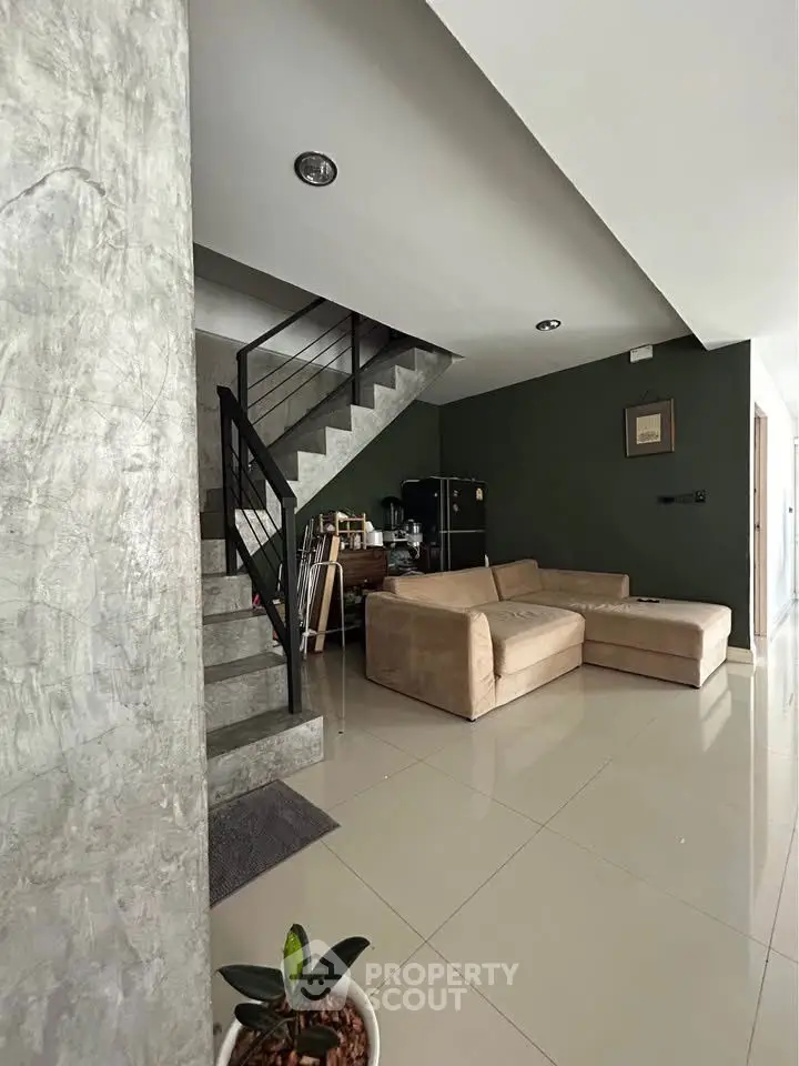 Modern living room with stylish staircase and cozy beige sectional sofa.