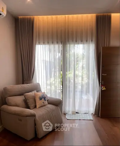 Cozy living room with plush armchair and floor-to-ceiling windows overlooking greenery.