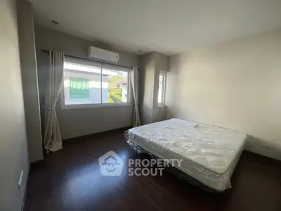 Spacious bedroom with large window and air conditioning, featuring a comfortable mattress on wooden flooring.