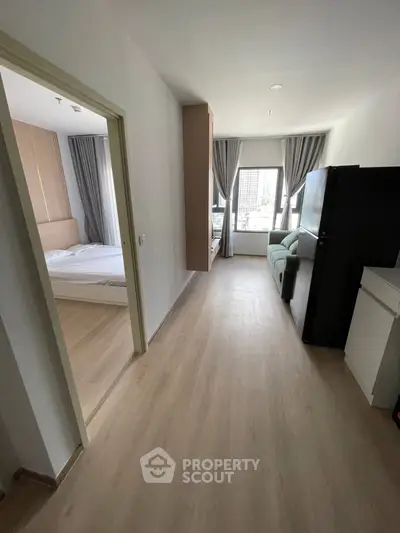Modern apartment interior with bedroom and living area, featuring large windows and light wood flooring.