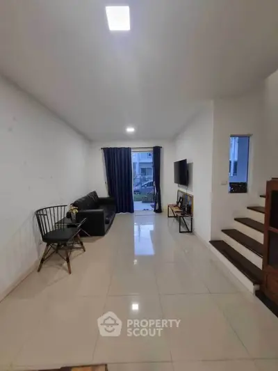 Spacious living room with modern decor and natural light, featuring a sleek black sofa and wall-mounted TV.