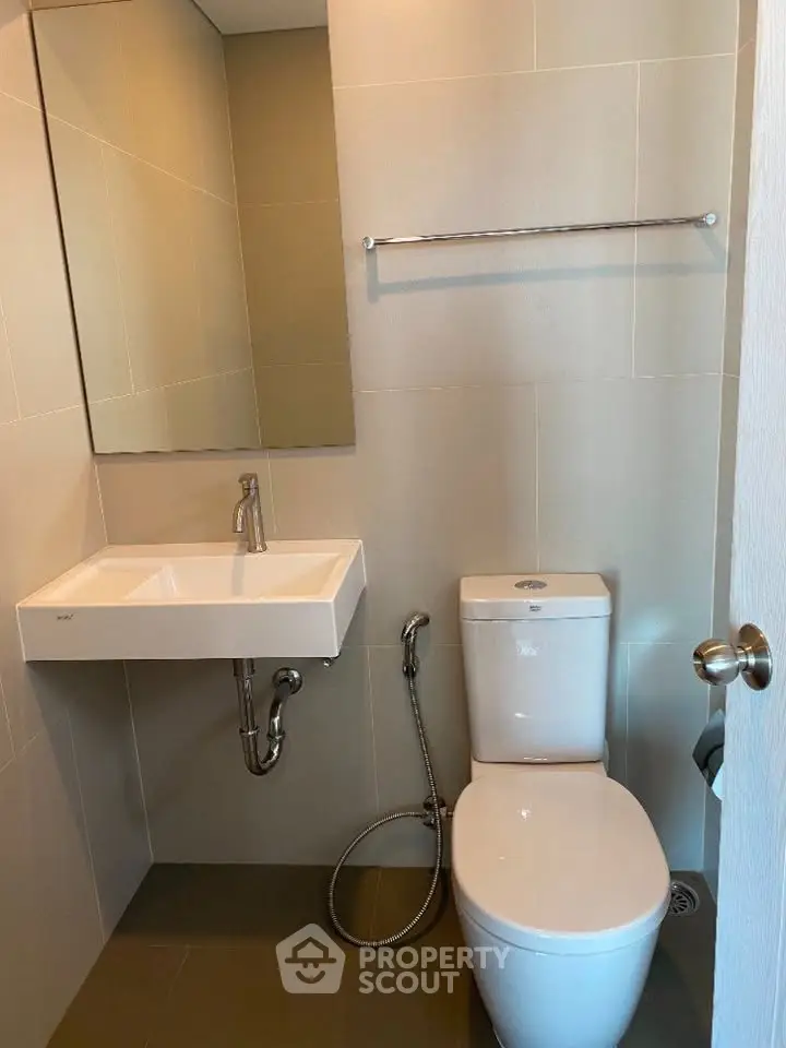 Modern bathroom with sleek fixtures and neutral tiles, featuring a wall-mounted sink and toilet.