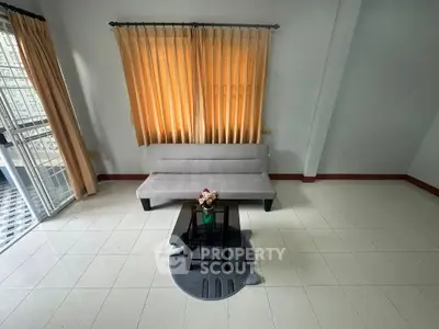 Spacious living room with modern sofa and glass coffee table, featuring large windows for natural light.