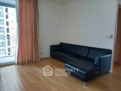 Spacious living room with sleek black leather sofa and wooden flooring, adjacent to a balcony with city view.