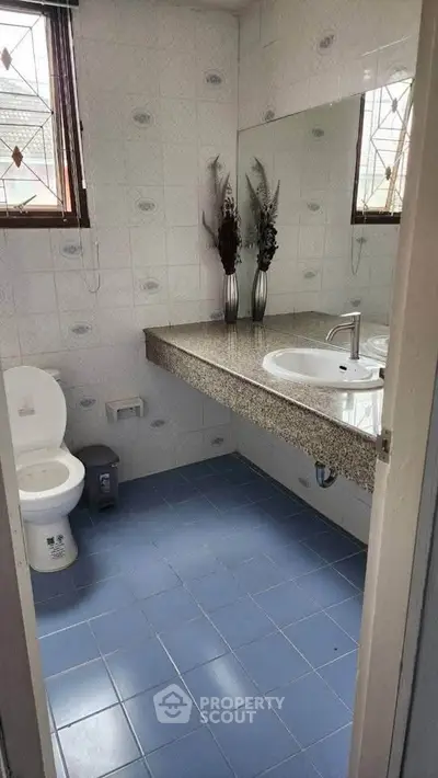 Modern bathroom with blue tiles and large mirror, featuring a sleek sink and toilet.