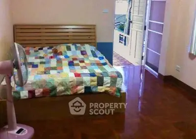 Cozy bedroom with colorful quilt and wooden flooring, featuring an open door to a balcony.