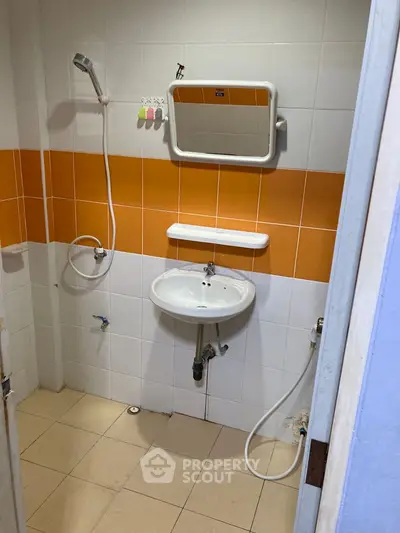 Compact bathroom with orange and white tiles, featuring a wall-mounted sink and mirror.