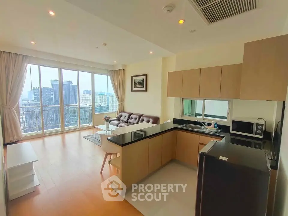 Modern open-layout living room with kitchen, large windows, and city view in high-rise apartment.