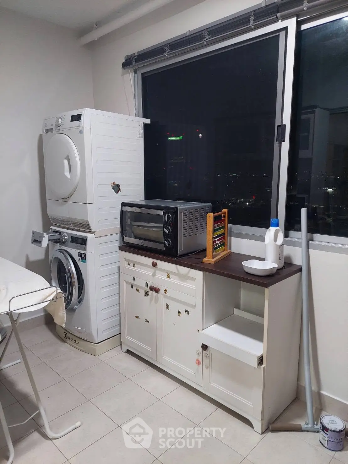 Modern laundry room with stacked washer dryer and city view, featuring a compact oven and storage cabinet.