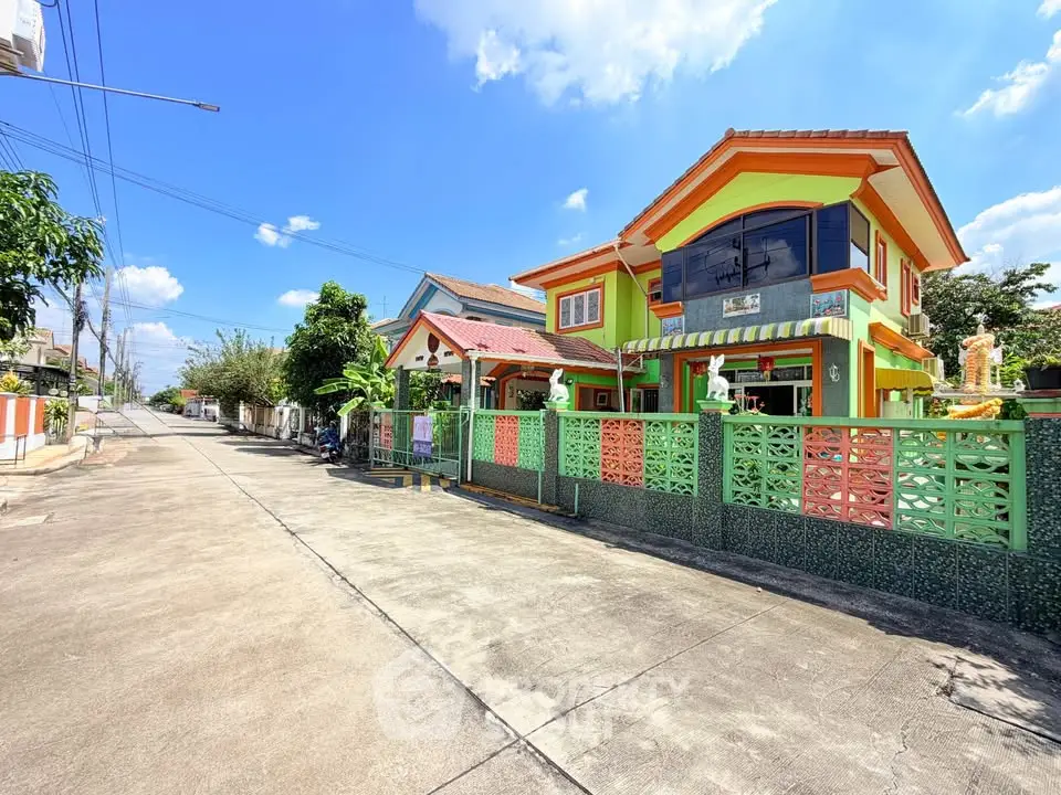 Vibrant two-story house with colorful facade and gated driveway in sunny suburban neighborhood.