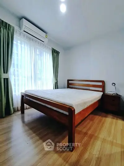 Spacious bedroom with wooden flooring and large window, featuring a comfortable bed and air conditioning.