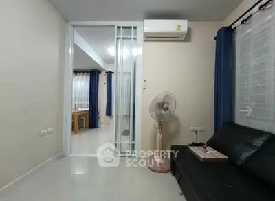 Spacious living room with modern decor and sliding glass door, featuring a comfortable black sofa and air conditioning.