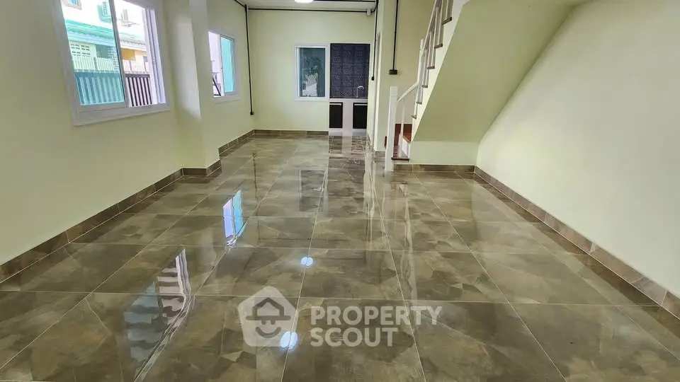 Spacious tiled living area with staircase and large windows in modern home.