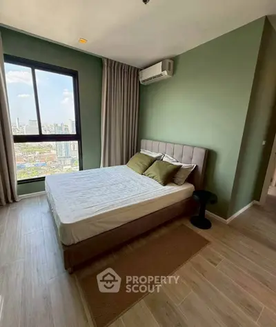 Modern bedroom with green walls, large window, and air conditioning in urban apartment.