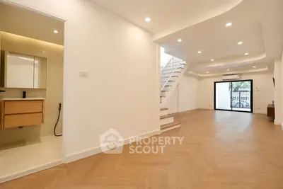 Spacious modern living room with wooden flooring and staircase, featuring open layout and ample natural light.