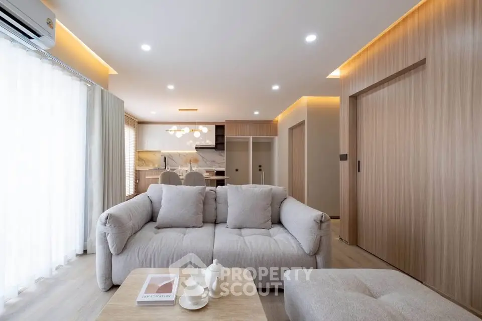 Modern living room with cozy sofa and open kitchen layout, featuring elegant lighting and wooden accents.