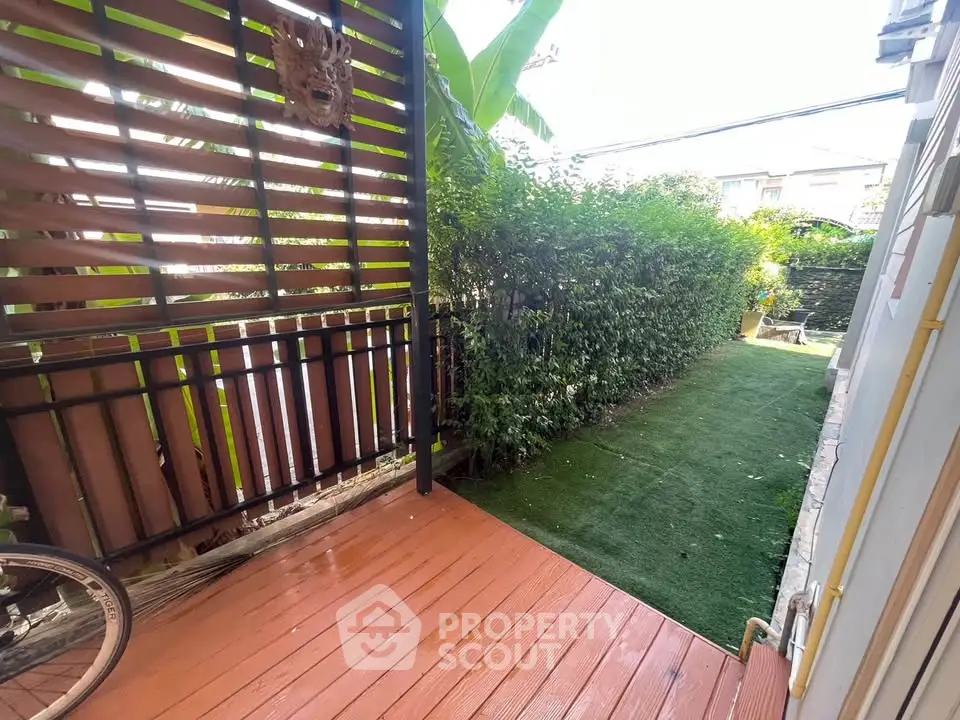 Charming garden patio with lush greenery and wooden deck, perfect for relaxation.