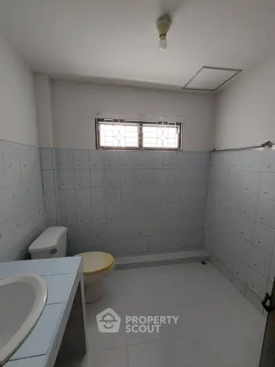 Spacious bathroom with tiled walls and natural light from window.