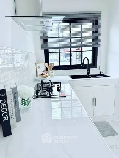 Modern kitchen with sleek white countertops and gas stove, featuring stylish decor and natural light.