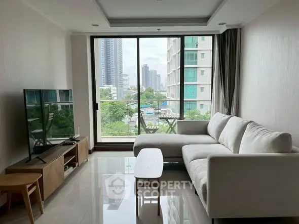 Modern living room with large window and city view, featuring a cozy white sofa and sleek TV setup.