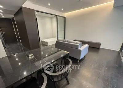 Modern open-plan living room with sleek dining area and cozy seating, featuring dark wood flooring and minimalist design.