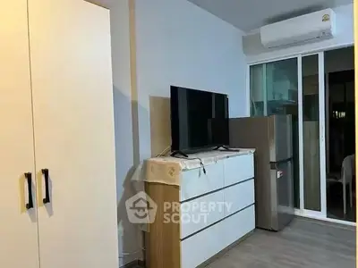 Modern apartment interior with TV, dresser, and air conditioning unit near sliding glass doors.