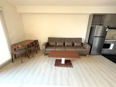 Modern living room with brown leather sofa, dining table, and stainless steel fridge in open layout.