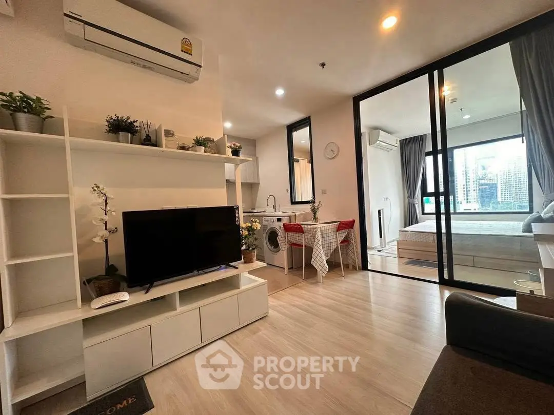 Modern open-plan living room with TV, dining area, and bedroom view in a stylish apartment.