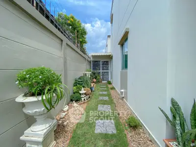 Charming garden pathway beside modern home with lush greenery and decorative planters.