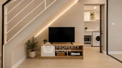 Modern living room with sleek TV stand and view into stylish kitchen with washing machine.