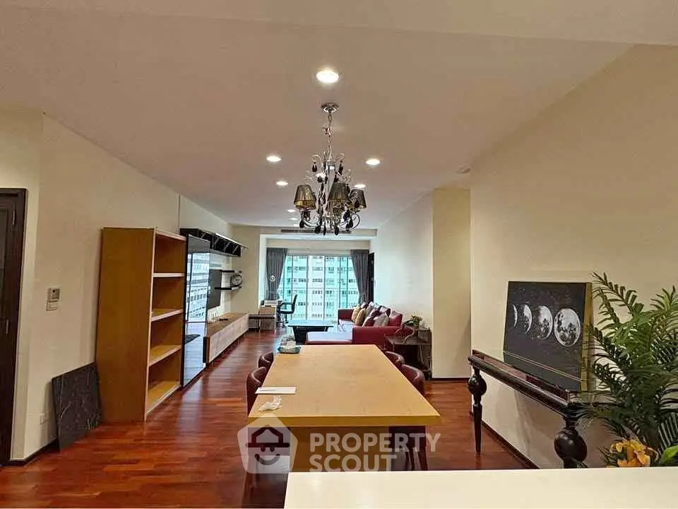 Spacious living room with elegant chandelier and city view, featuring hardwood floors and modern decor.