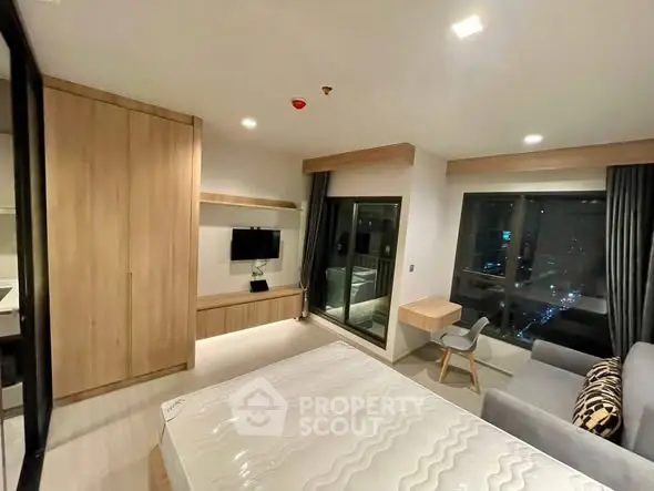 Modern bedroom with city view, featuring sleek furniture and large windows for natural light.