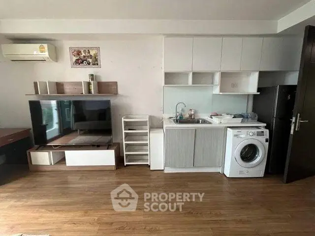 Modern studio apartment with wooden flooring, compact kitchen, and washing machine.