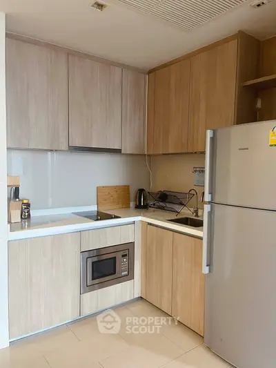 Modern kitchen with sleek cabinetry, built-in microwave, and stainless steel fridge in a cozy apartment.