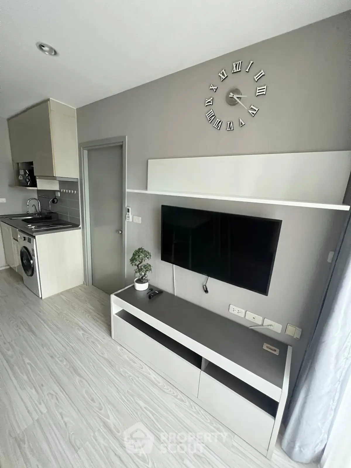 Modern living room with sleek design, wall-mounted TV, and compact kitchen featuring washing machine.