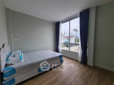 Spacious bedroom with large window and wooden flooring in modern apartment
