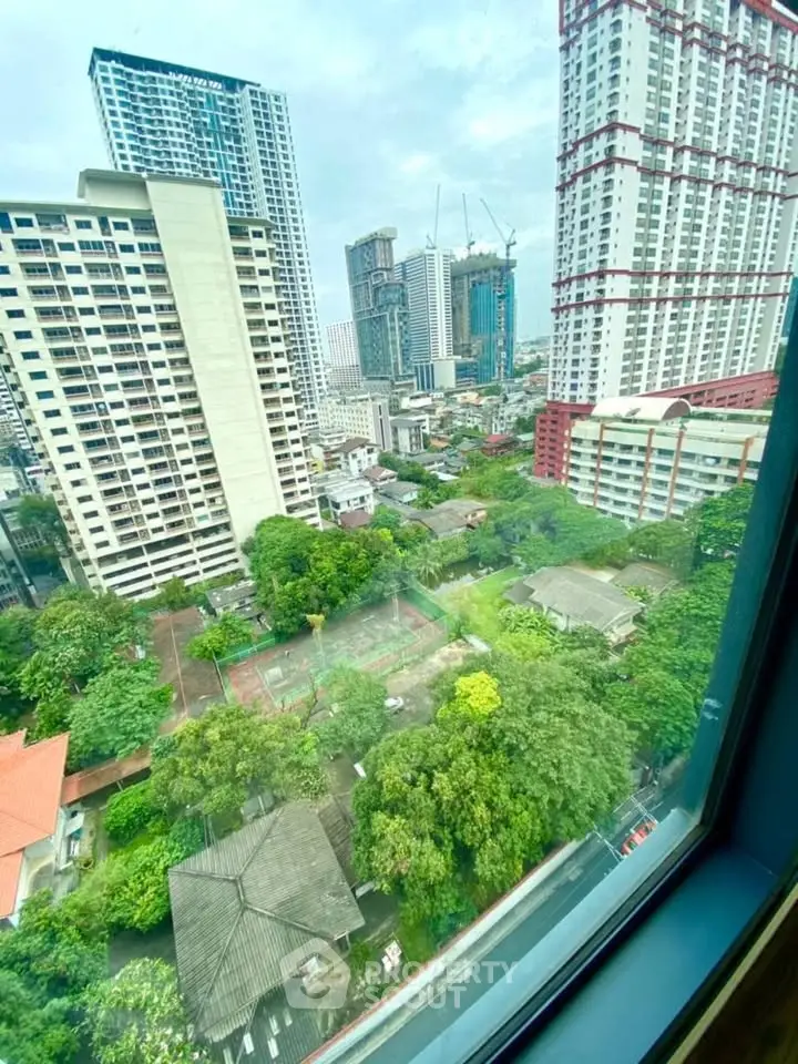 Stunning cityscape view from high-rise apartment window showcasing urban skyline and lush greenery.