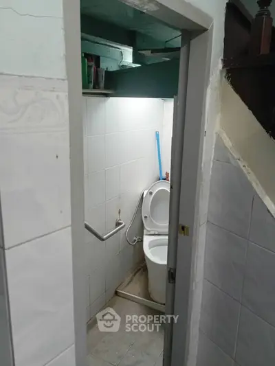 Compact bathroom with white tiles and toilet under staircase